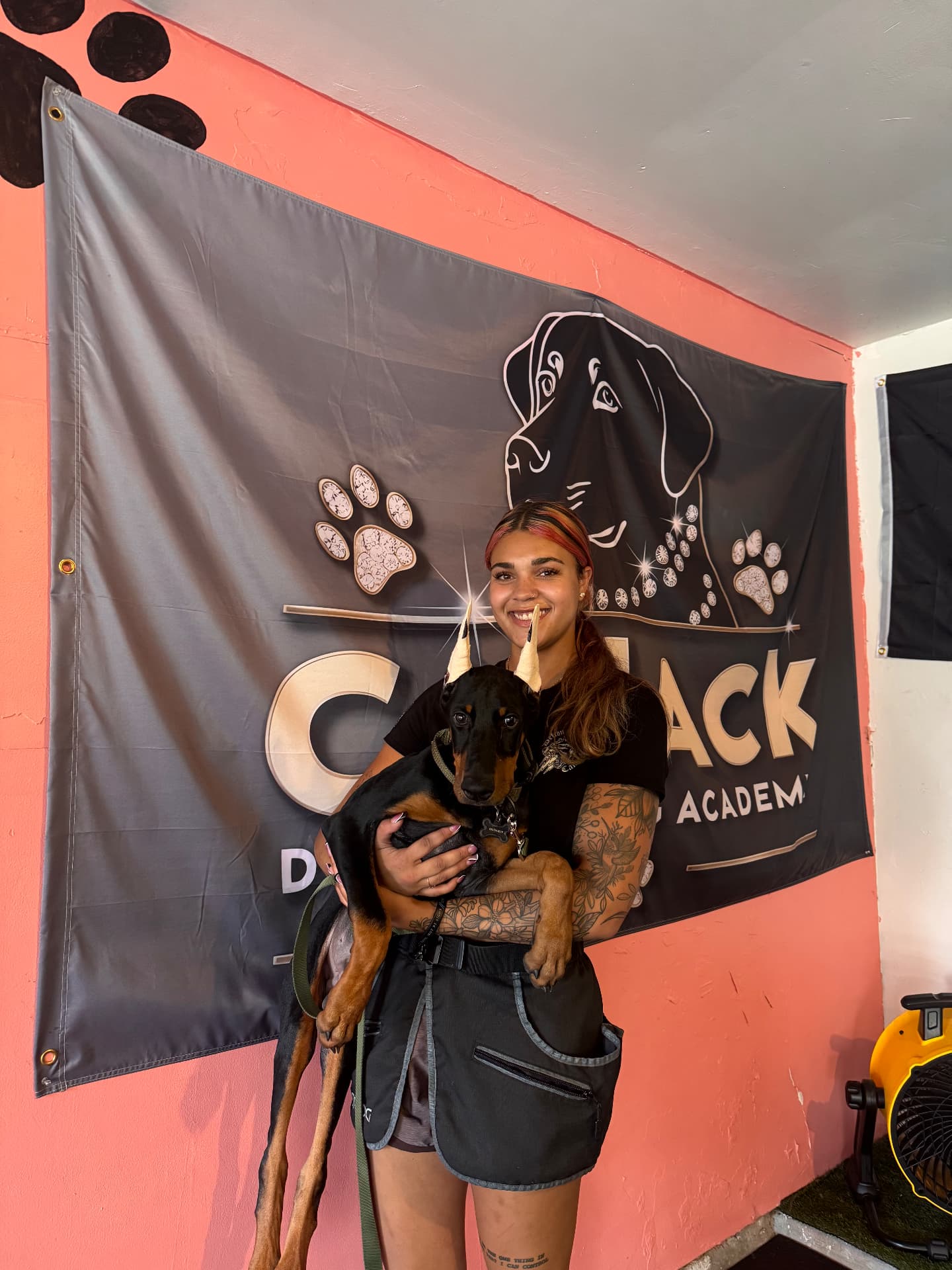 Cat Jackson holding a Doberman puppy in front of the CatJack K9 Academy banner